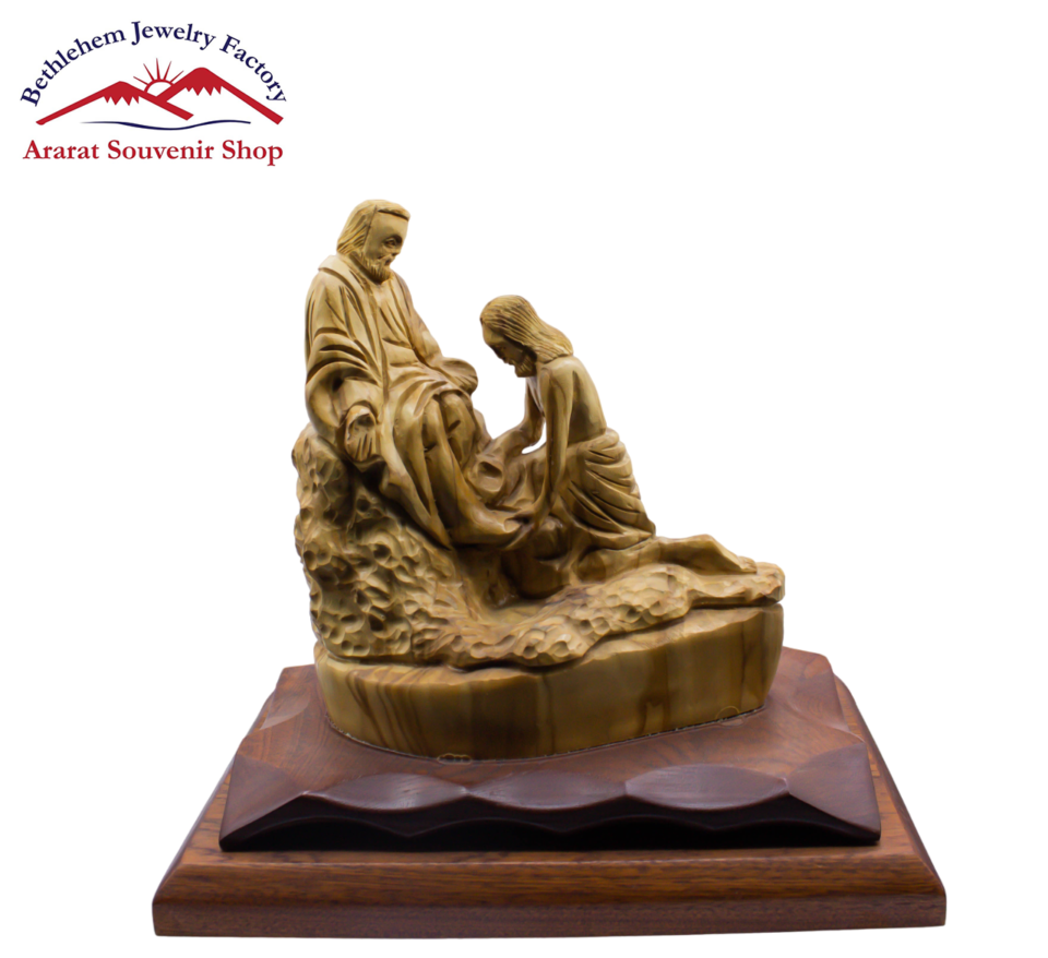 A statue of Jesus washing the disciples' feet and a woman on a wooden base, depicting a moment of discipleship.